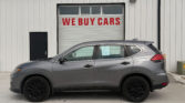 Gray SUV parked in front of a white corrugated metal building with a large red 'WE BUY CARS' sign on the garage door.
