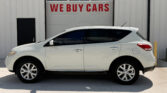 White SUV parked in front of a gray industrial building with a large garage door reading WE BUY CARS.