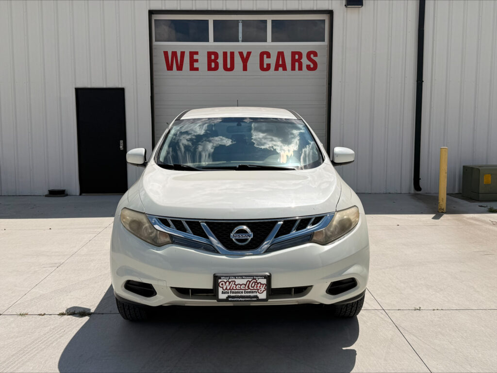 White Nissan SUV parked in front of a garage door reading 'WE BUY CARS'