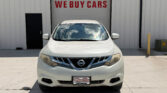 White Nissan SUV parked in front of a garage door reading 'WE BUY CARS'