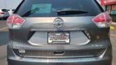 Rear view of a gray Nissan Rogue SUV with a Wheel City Auto Finance Centers plate frame in a parking lot; green dealership sticker on rear window and a storefront sign in the background: 'We Finance'