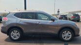 Side view of a silver SUV with roof rails parked in a lot, other cars and an industrial building visible in the background