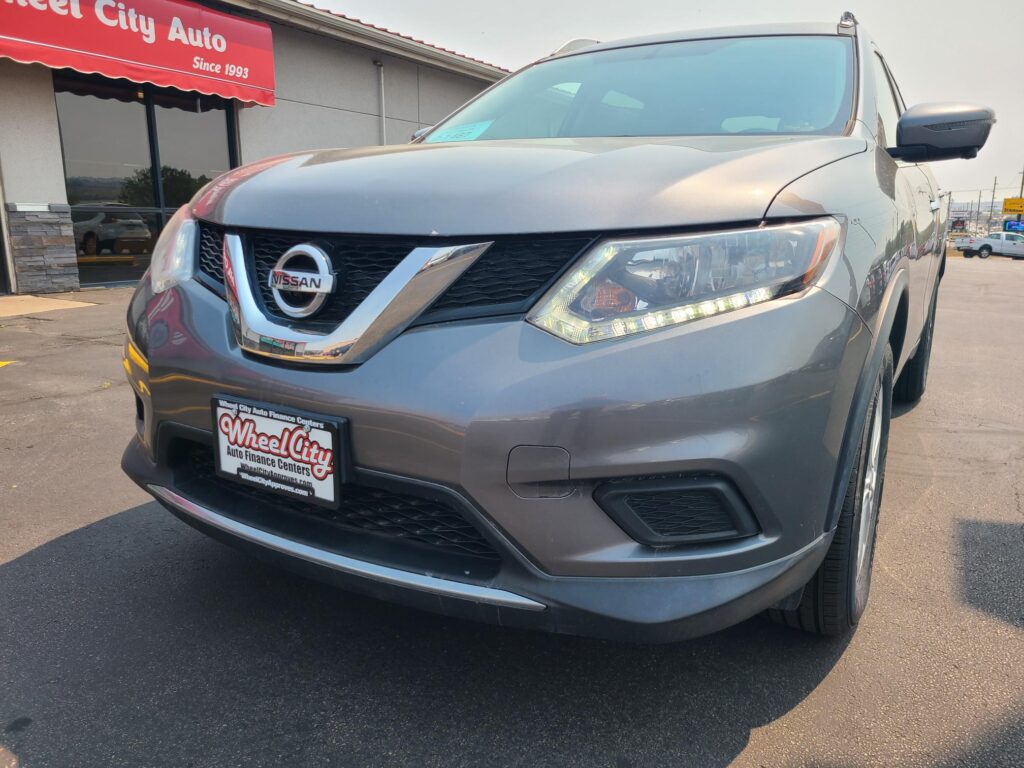 Front view of a gray Nissan SUV parked outside Wheel City Auto dealership with a red sign overhead reading 'Wheel City Auto'