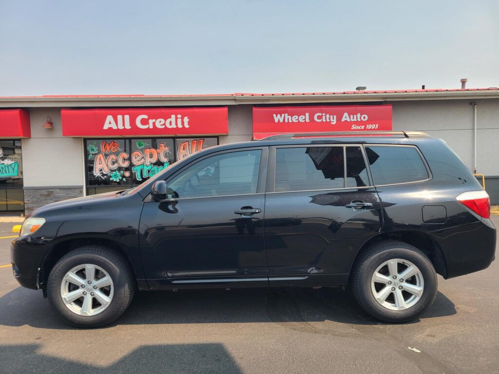 Front of a storefront with red signs reading 'All Credit' and 'Wheel City Auto', and a dark SUV parked in front.