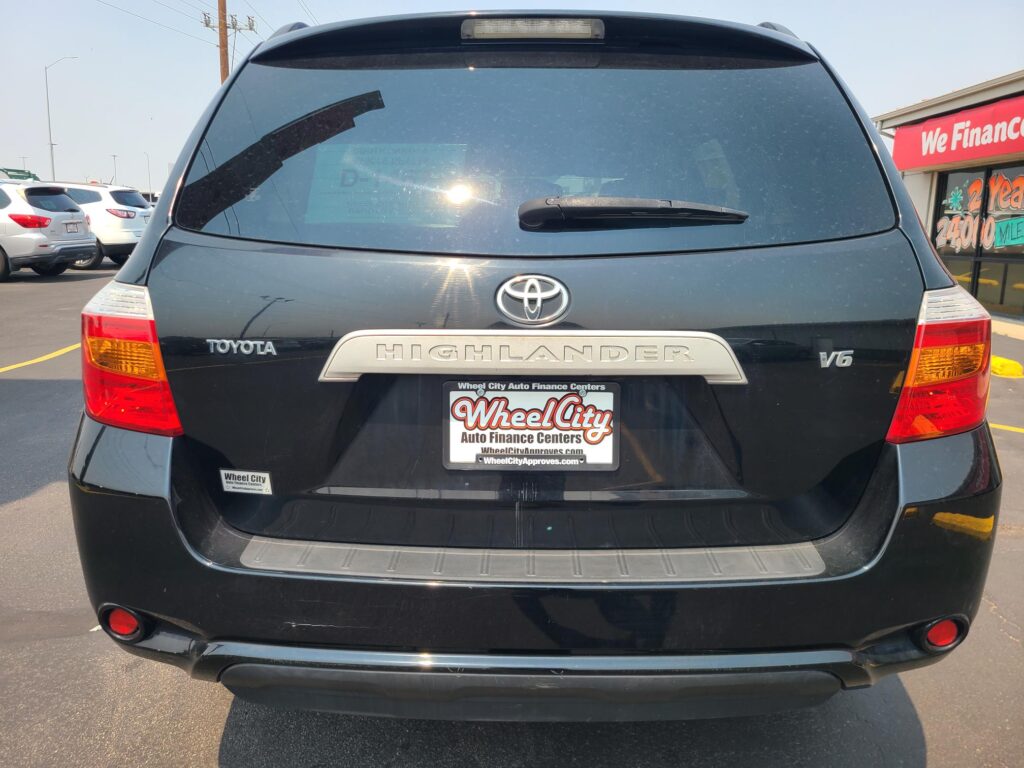 Rear view of a dark gray Toyota Highlander SUV in a parking lot, showing the tail lights, rear window wiper, and Wheel City license plate frame.