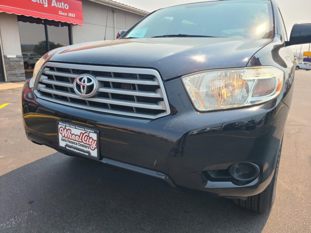 Front view of a dark blue Toyota vehicle at Wheel City Auto Finance Centers dealership, with a red 'City Auto Since 1993' awning in the background