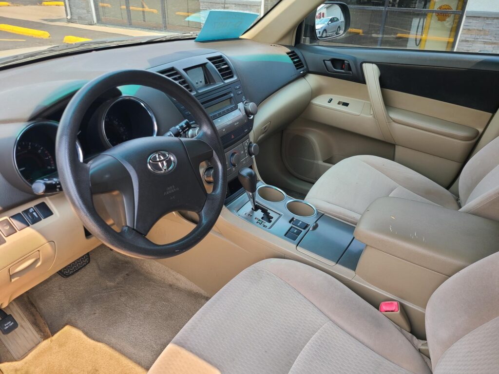 Beige Toyota car interior with steering wheel, dashboard, center console, gear shifter, and cupholders visible between front seats.