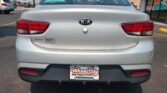 Rear view of a silver Kia Rio in a dealership lot, with Wheel City license plate frame and a 'We Finance' storefront in the background.