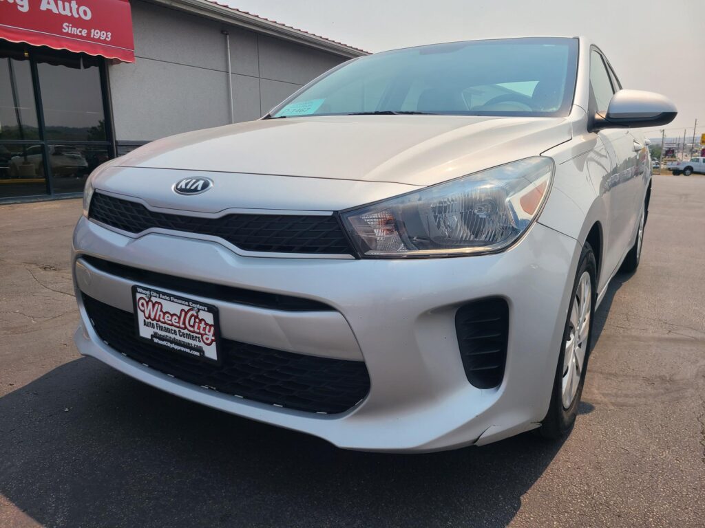 Front-left view of a white Kia sedan at a car dealership, Wheel City Auto Finance Centers license plate frame visible in the foreground.