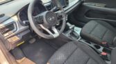 Front interior of a Kia: steering wheel, instrument cluster, center touchscreen, gear shifter, and black cloth seats in view.