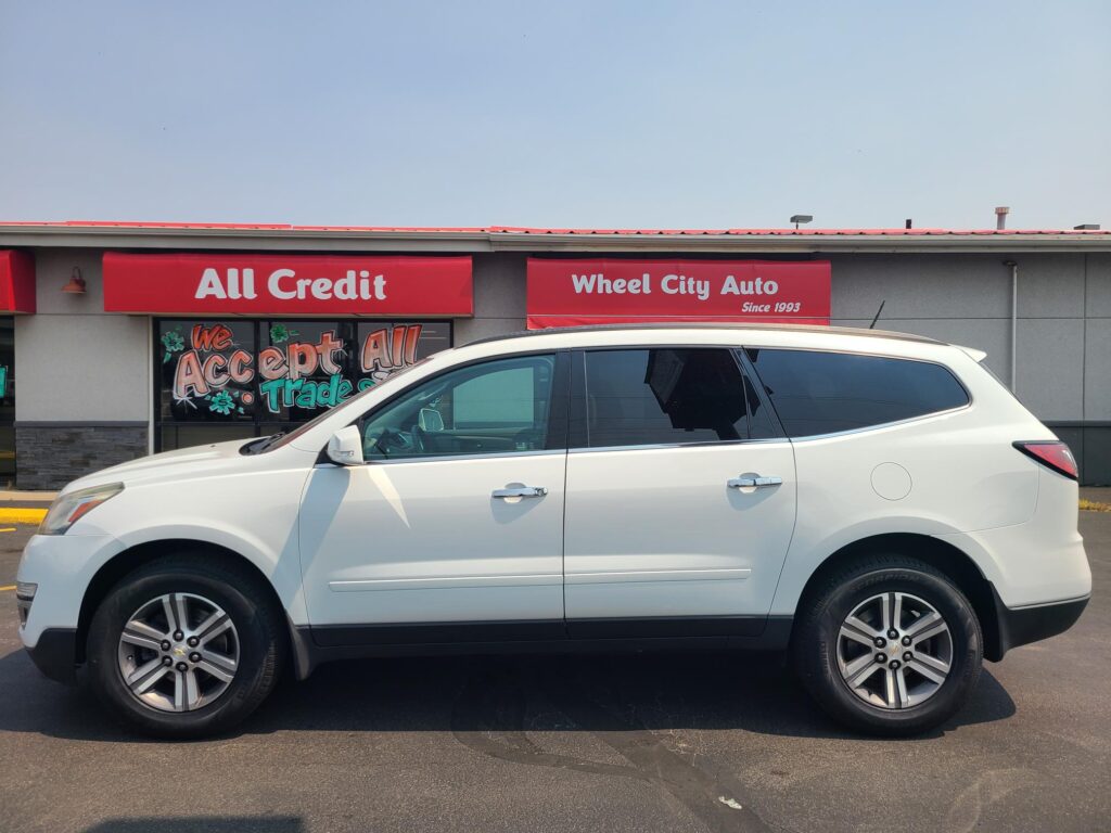 White SUV parked in front of a car dealership with red banners reading 'All Credit' and 'Wheel City Auto'