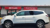 White SUV parked in front of a car dealership with red banners reading 'All Credit' and 'Wheel City Auto'