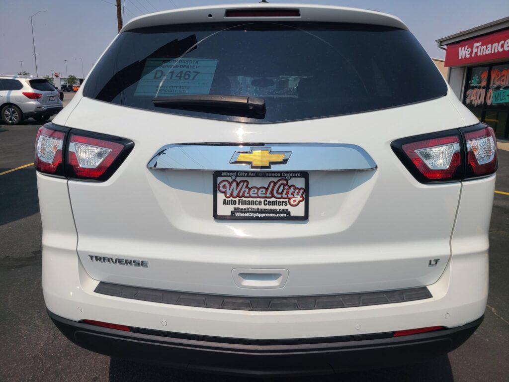 Rear view of a white Chevrolet Traverse LT at a car dealership, showing the Wheel City Auto Finance Centers plate frame and a 'We Finance' sign on the side window.