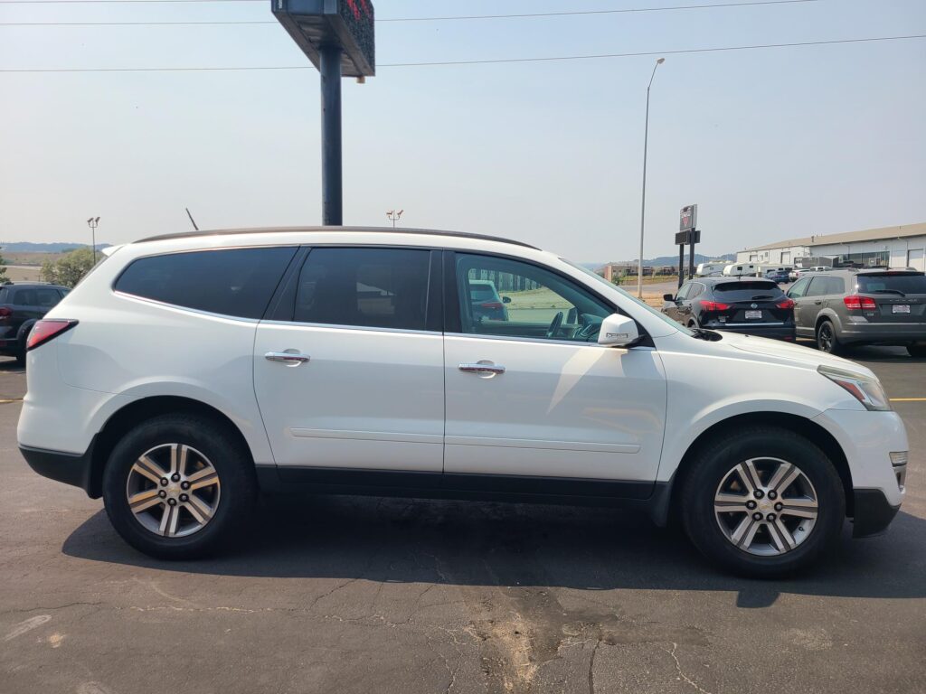 White SUV parked in a lot, side view, with other cars and a warehouse in the background.