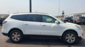 White SUV parked in a lot, side view, with other cars and a warehouse in the background.
