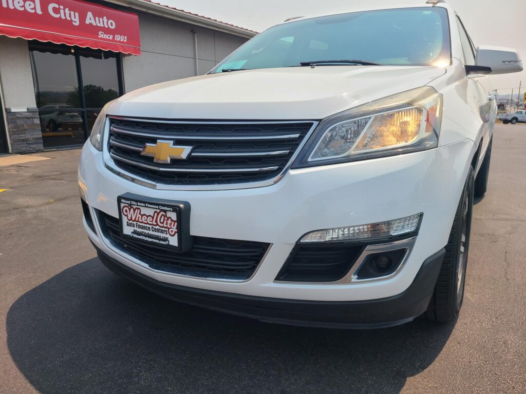 Front view of a white Chevrolet SUV in a car lot, with the vehicle's grille and headlight visible near a Wheel City Auto dealership sign.