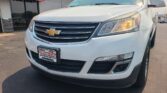 Front view of a white Chevrolet SUV in a car lot, with the vehicle's grille and headlight visible near a Wheel City Auto dealership sign.