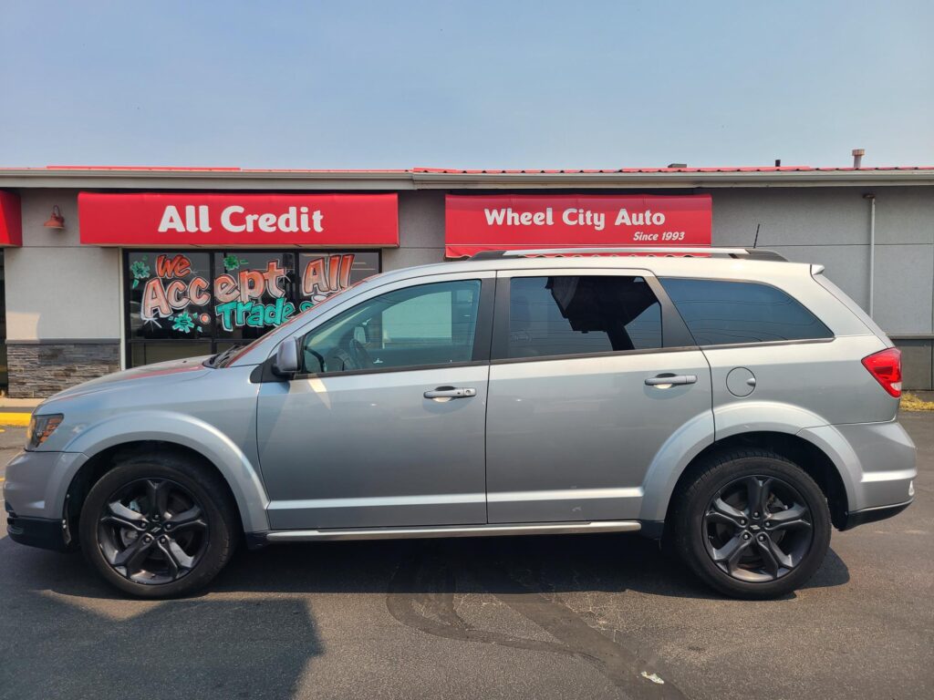 Front view of an auto shop with red signs reading 'All Credit' and 'Wheel City Auto' and a silver SUV parked in front.