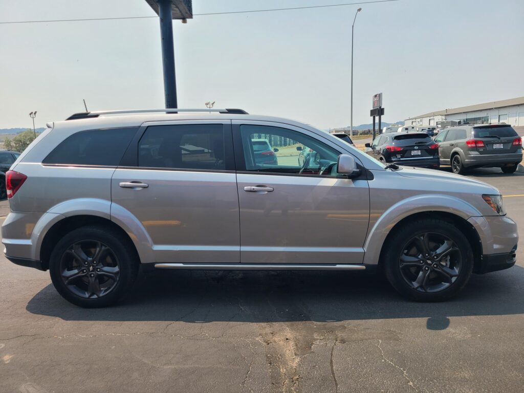 Silver SUV parked in a lot, shown in profile with other vehicles and a warehouse in the distance.