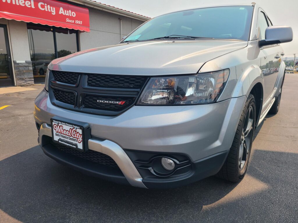 Close-up of the front end of a silver Dodge SUV at a car dealership, Wheel City Auto visible on the storefront sign and license plate frame.