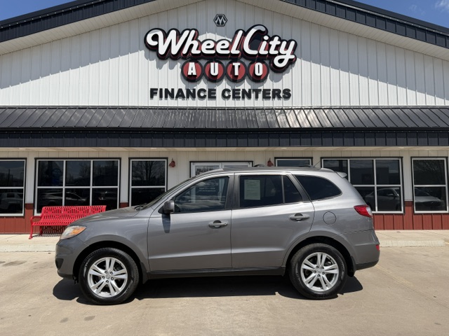 Silver SUV parked in front of Wheel City Auto Finance Centers storefront with large sign and a red bench nearby.