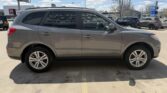 Gray crossover SUV seen in profile, parked in a lot with other vehicles and clear blue sky above.