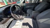 Front interior of a gray Hyundai SUV from the driver’s side, showing the steering wheel, dashboard gauges, center console with gear shifter and cup holders, and front seats with sunlight streaming in.