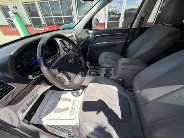 Front interior of a gray Hyundai SUV from the driver’s side, showing the steering wheel, dashboard gauges, center console with gear shifter and cup holders, and front seats with sunlight streaming in.