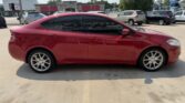 Red four‑door sedan parked in a parking lot, with tinted windows and alloy wheels, side view.