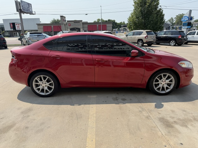 Red four‑door sedan parked in a parking lot, with tinted windows and alloy wheels, side view.