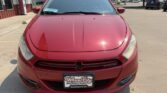 Front view of a red Dodge sedan parked in a lot, dealership building and other cars visible in the background.
