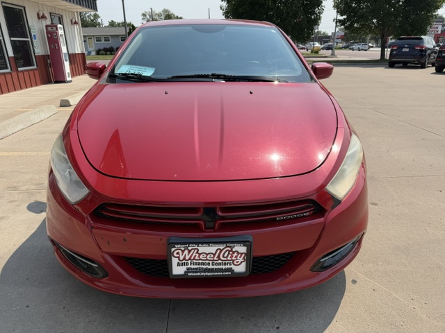 Front view of a red Dodge sedan parked in a lot, dealership building and other cars visible in the background.