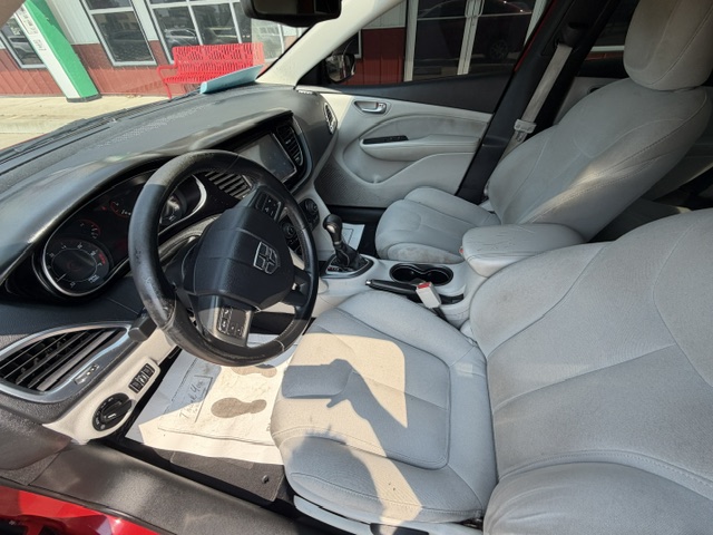 Interior view of a gray car: steering wheel, center console with gear shifter, and front seats visible in daylight