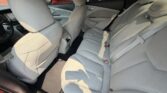 Light gray fabric rear seats in a sedan with three seat belts and headrests, photographed from the rear passenger side door open.