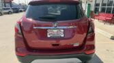 Rear view of a red Buick Encore SUV parked in a dealership lot; Buick emblem on the tailgate, 'Encore' badge visible, license plate frame reads 'Wheel City Auto Finance Centers' with surrounding dealership signage in the background.