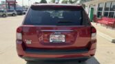 Rear view of a red Jeep SUV parked in a lot, showing the 4x4 badge and a Wheel City dealership plate on the back.