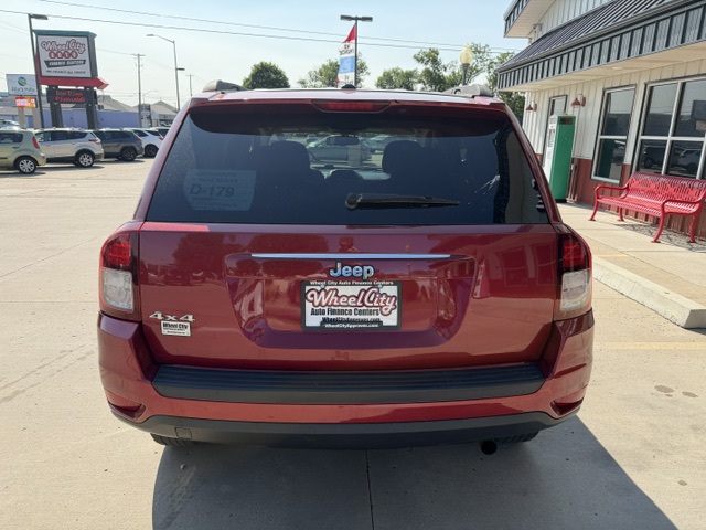Rear view of a red Jeep SUV parked in a lot, showing the 4x4 badge and a Wheel City dealership plate on the back.