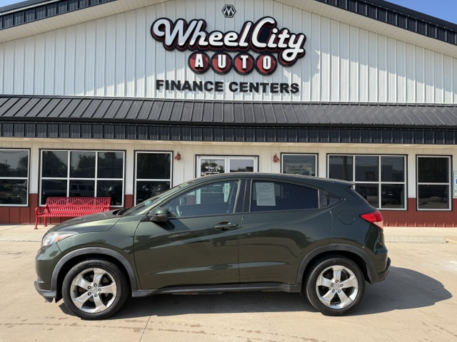 Green SUV parked in front of Wheel City Auto Finance Centers storefront with a red bench nearby.