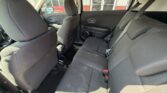 Rear interior of a car with black fabric seats, three-seat bench, headrests, and visible seat belts. Front seats also visible from the back seat area.