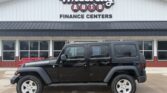 Black four-door Jeep Wrangler parked in front of Wheel City Auto Finance Centers storefront sign.