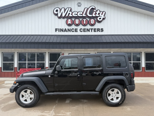 Black four-door Jeep Wrangler parked in front of Wheel City Auto Finance Centers storefront sign.