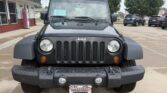 Front view of a black Jeep Wrangler with a seven-slot grille, round headlights, and a rugged bumper on a wet parking lot; dealership plate frame reads Wheel City Auto Finance Centers.