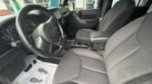 Front interior of a dark Jeep SUV showing the steering wheel, dashboard, center console, and two fabric front seats inside.