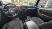 Front interior of a black Jeep with a steering wheel, touchscreen display, and center console visible from the passenger seat side at a dealership parking lot.