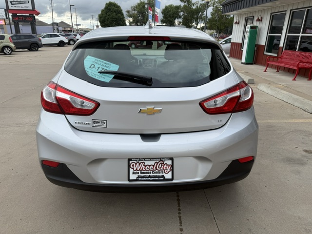 Rear view of a silver Chevrolet hatchback at a dealership, with a Wheel City license plate frame and a D-172 tag on the rear window.