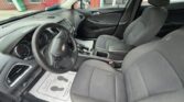 Interior view of a Chevrolet sedan showing the driver's seat, steering wheel, center console, and front passenger seat with a car dealership exterior visible through the windows.