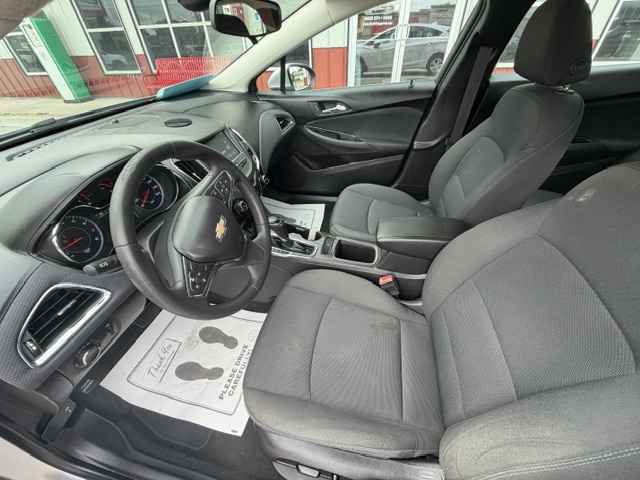 Interior view of a Chevrolet sedan showing the driver's seat, steering wheel, center console, and front passenger seat with a car dealership exterior visible through the windows.