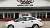 White sedan parked in front of a Wheel City Auto Finance Centers storefront with a red bench and large windows behind it.