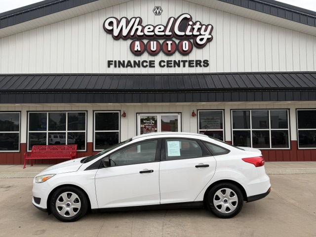 White sedan parked in front of a Wheel City Auto Finance Centers storefront with a red bench and large windows behind it.
