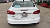 Rear view of a white Ford Focus in a dealership lot, with a Wheel City Auto Finance Centers plate and a blue sale sticker on the rear window.